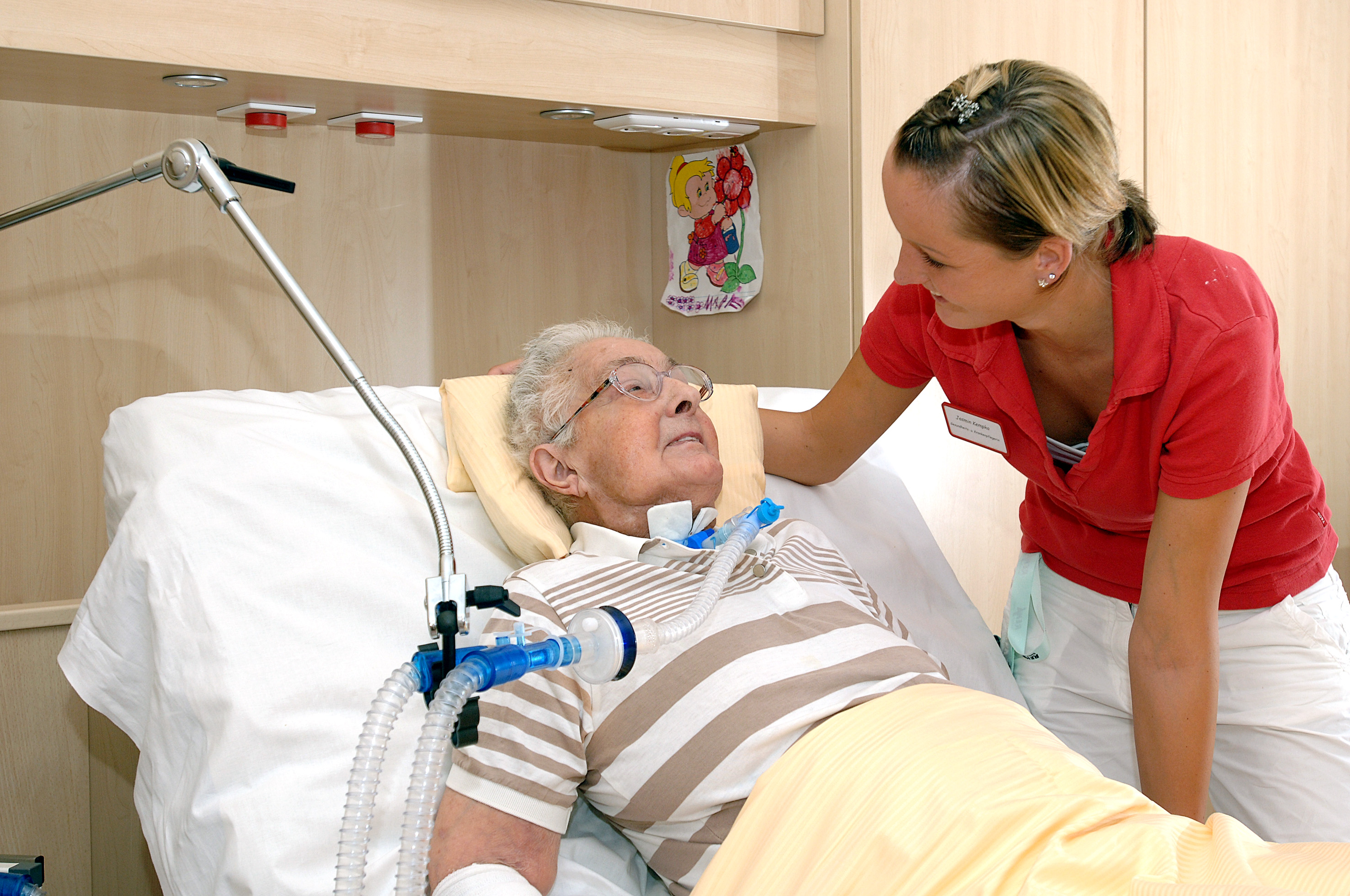 Eine Pflegerin beugt sich über einen Senior,der in einem Pflegebett liegt