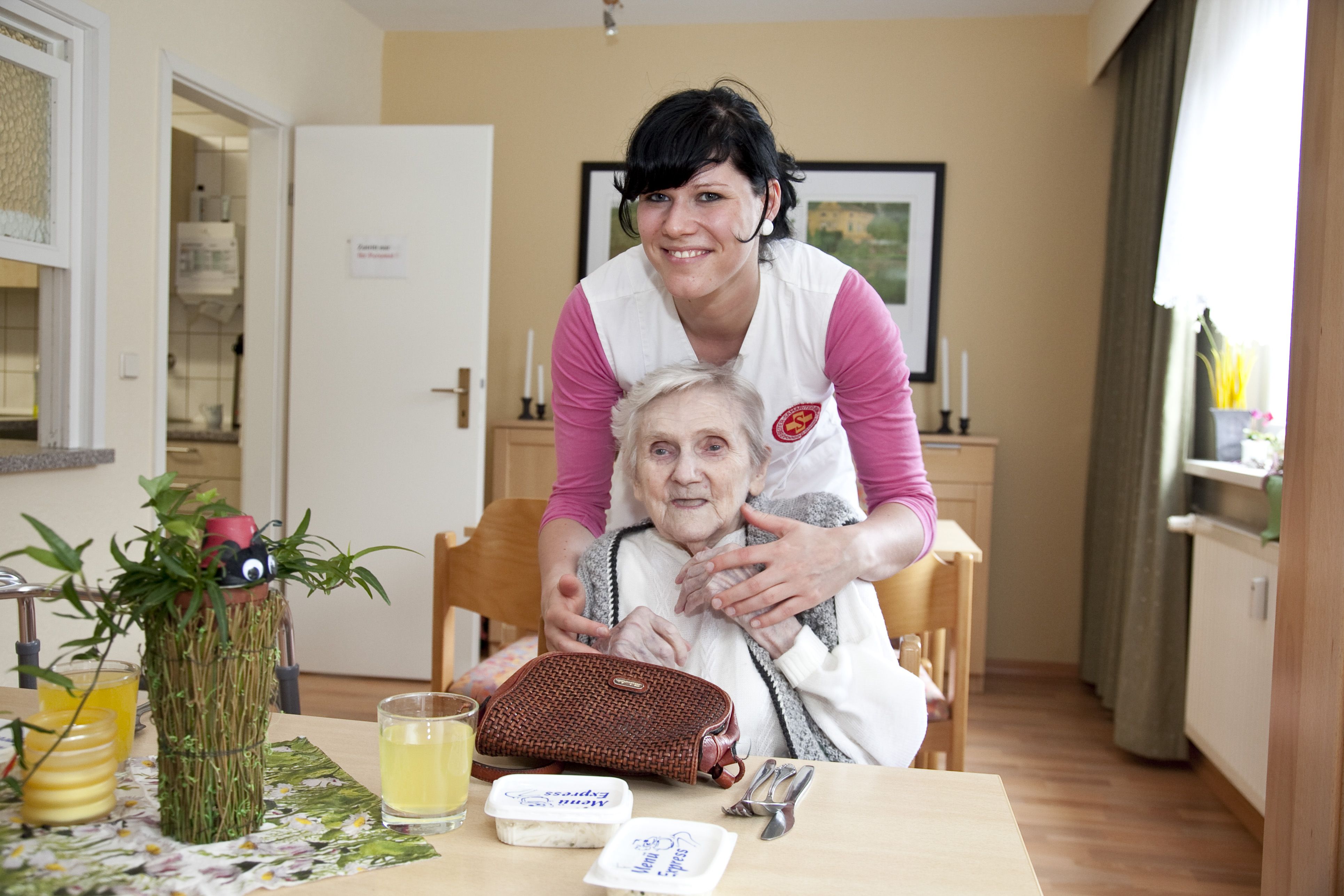 Eine Pflegerin umarmt eine alte Dame im Rollstuhl